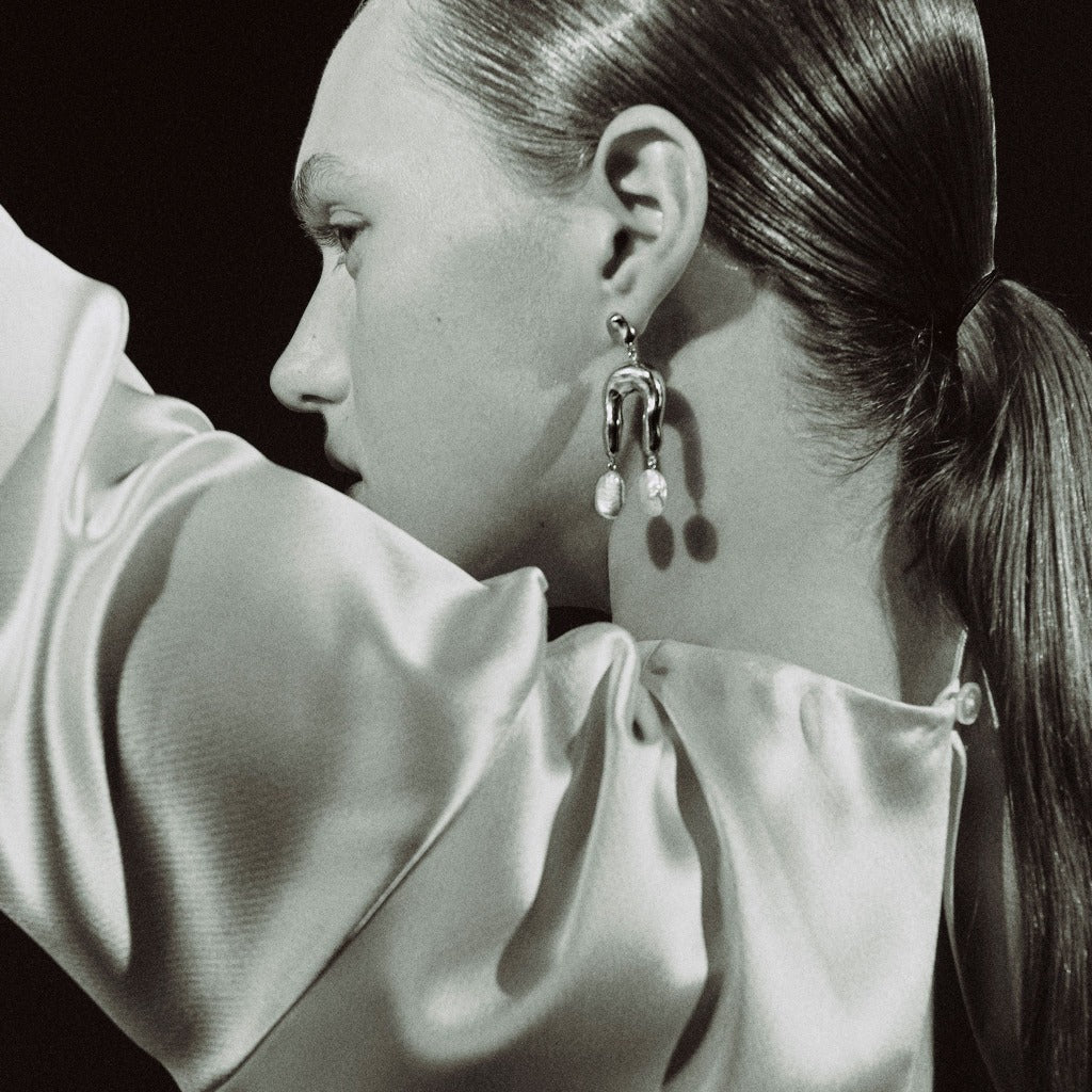 Woman wearing AGMES 0.925 sterling silver earrings with sculpted wishbone and freshwater pearl drop.