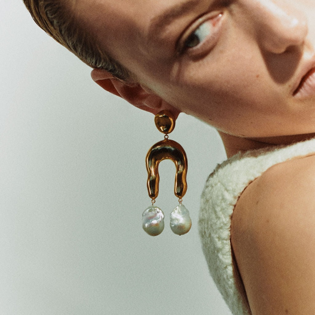 Woman wearing AGMES 18k gold vermeil earrings with sculpted wishbone and freshwater pearl drop.