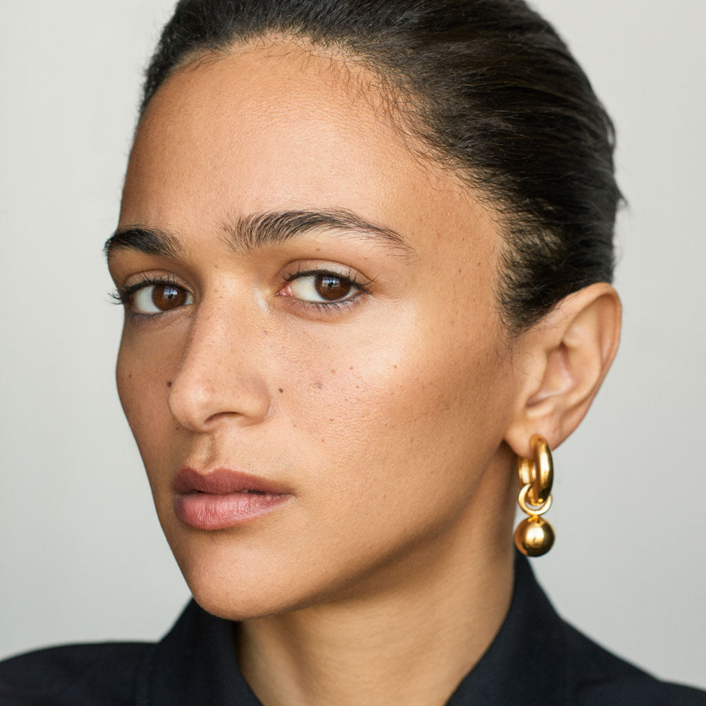 Woman wearing AGMES 0.925 sterling silver hinged hoop earrings with 18k yellow gold round embellishments.