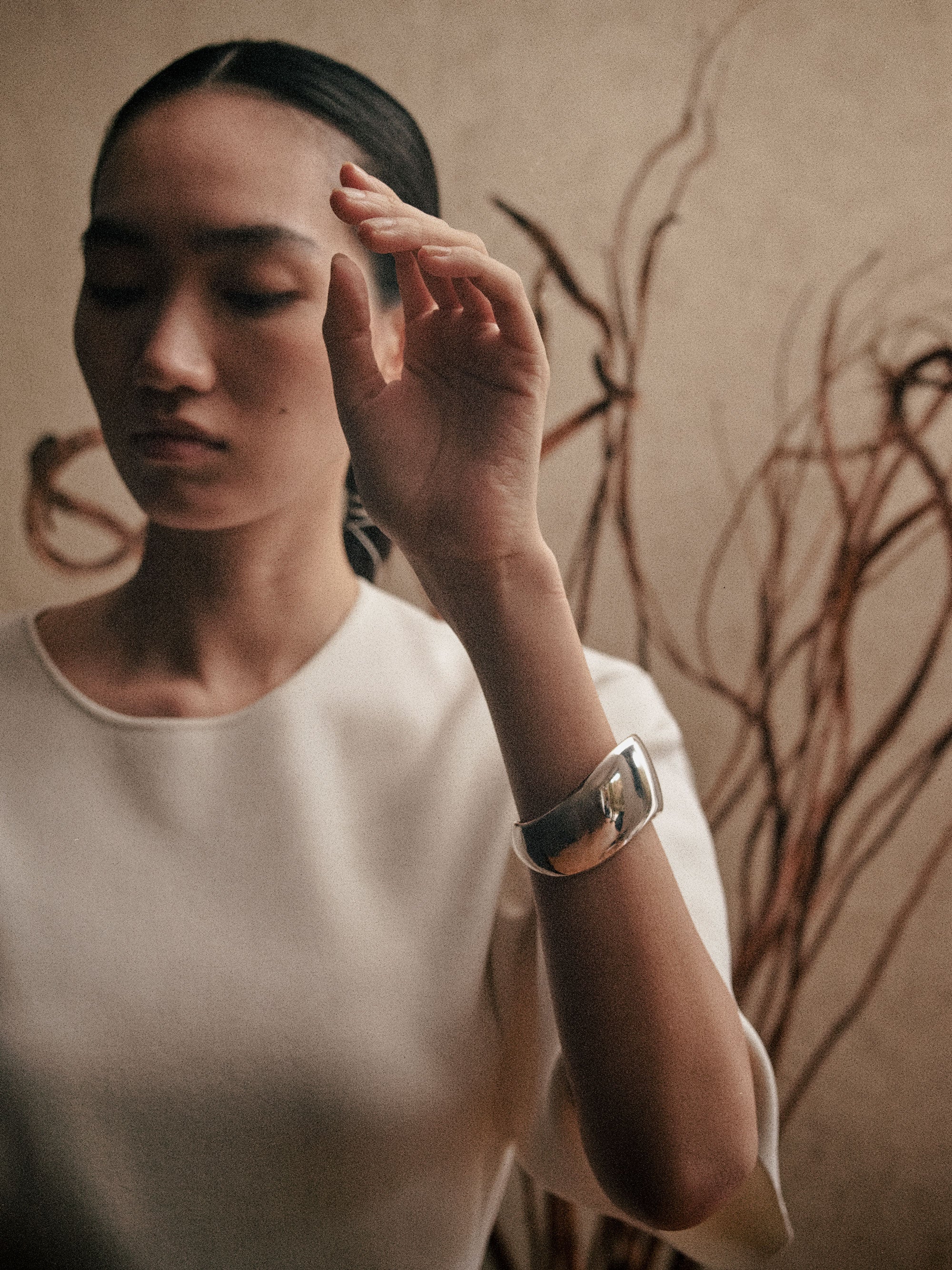 Woman wearing white blouse and AGMES 0.925 sterling silver sculpted Cecil cuff bracelet in front of natural background.
