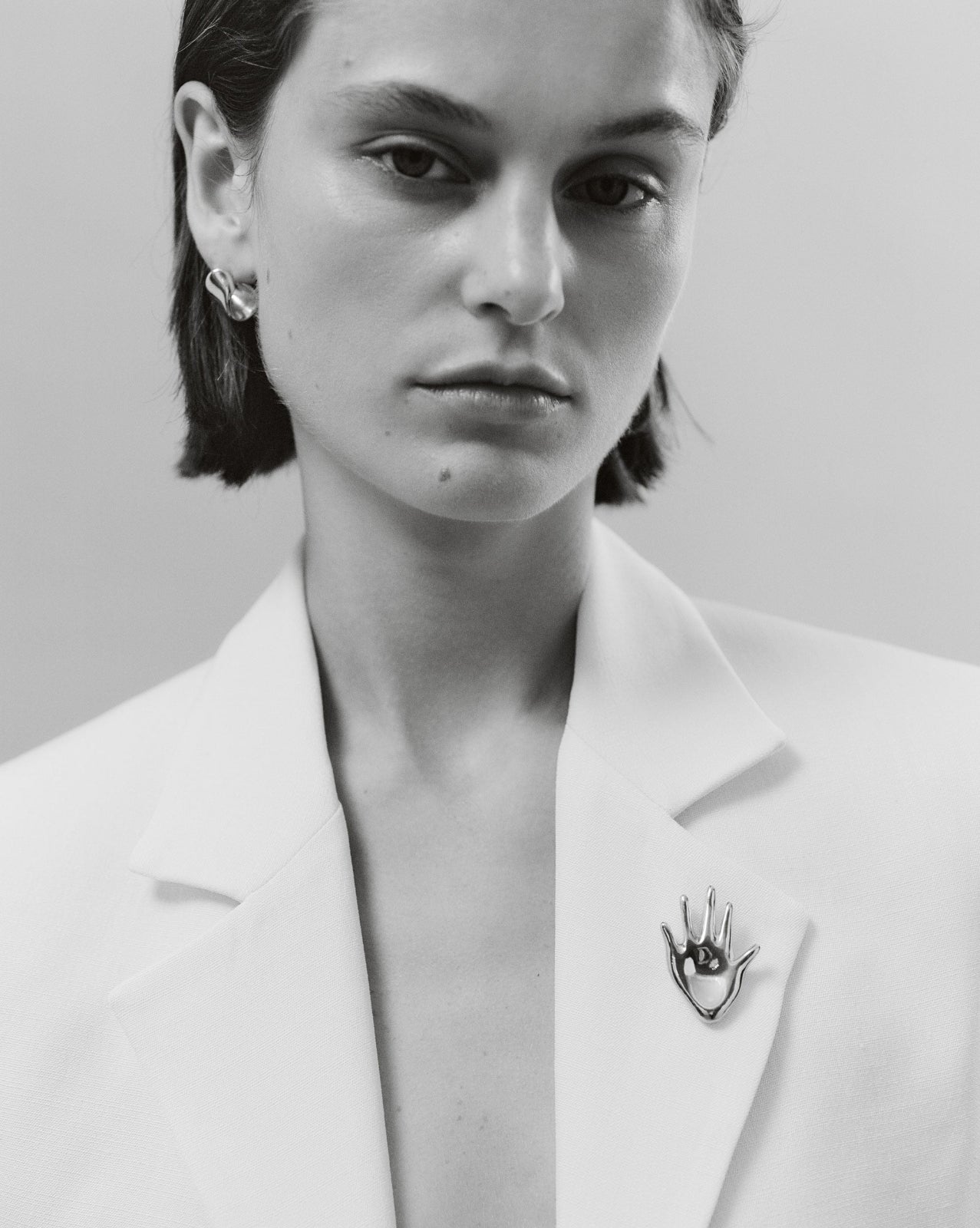 Woman wearing the AGMES .925 Sterling Silver Dali Brooch on white blazer and Nelle Earrings. Hand shaped Brooch. 