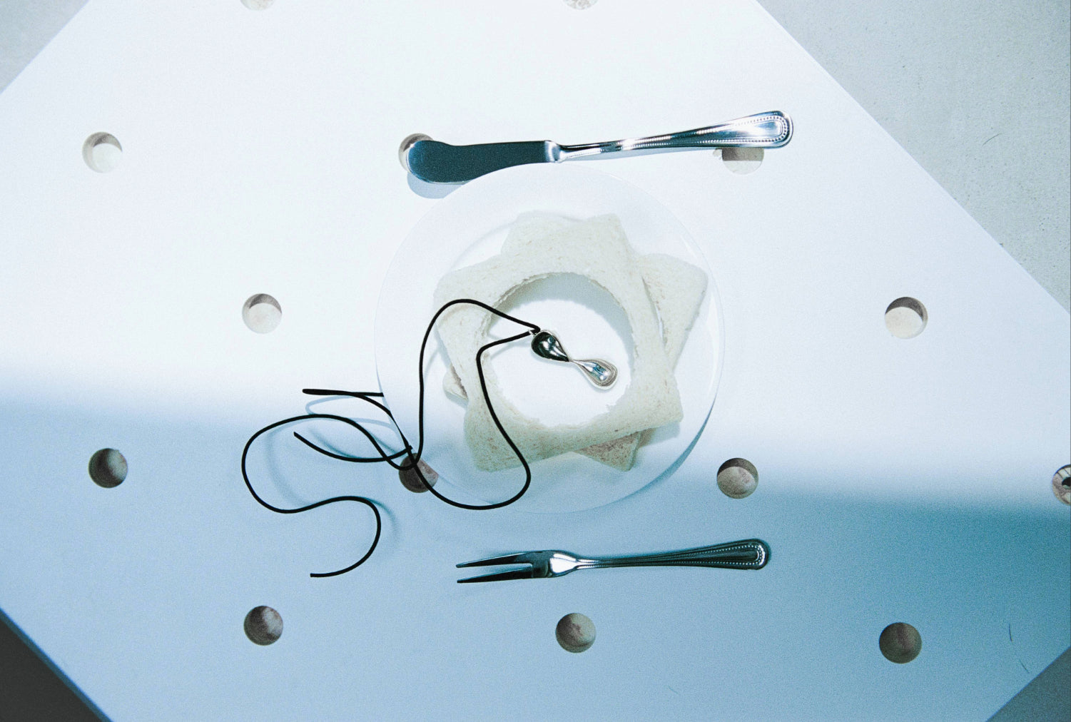 AGMES .925 sterling silver sculptural infinity Inti pendant with black suede cord on plate with silver fork and knife.