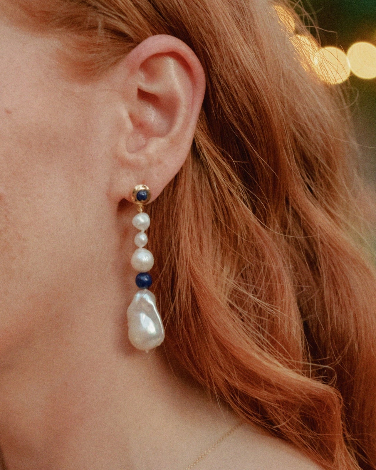 Person wearing AGMES 18K Gold Vermeil Kait Earrings with Baroque Pearl and Lapis Stone drop.