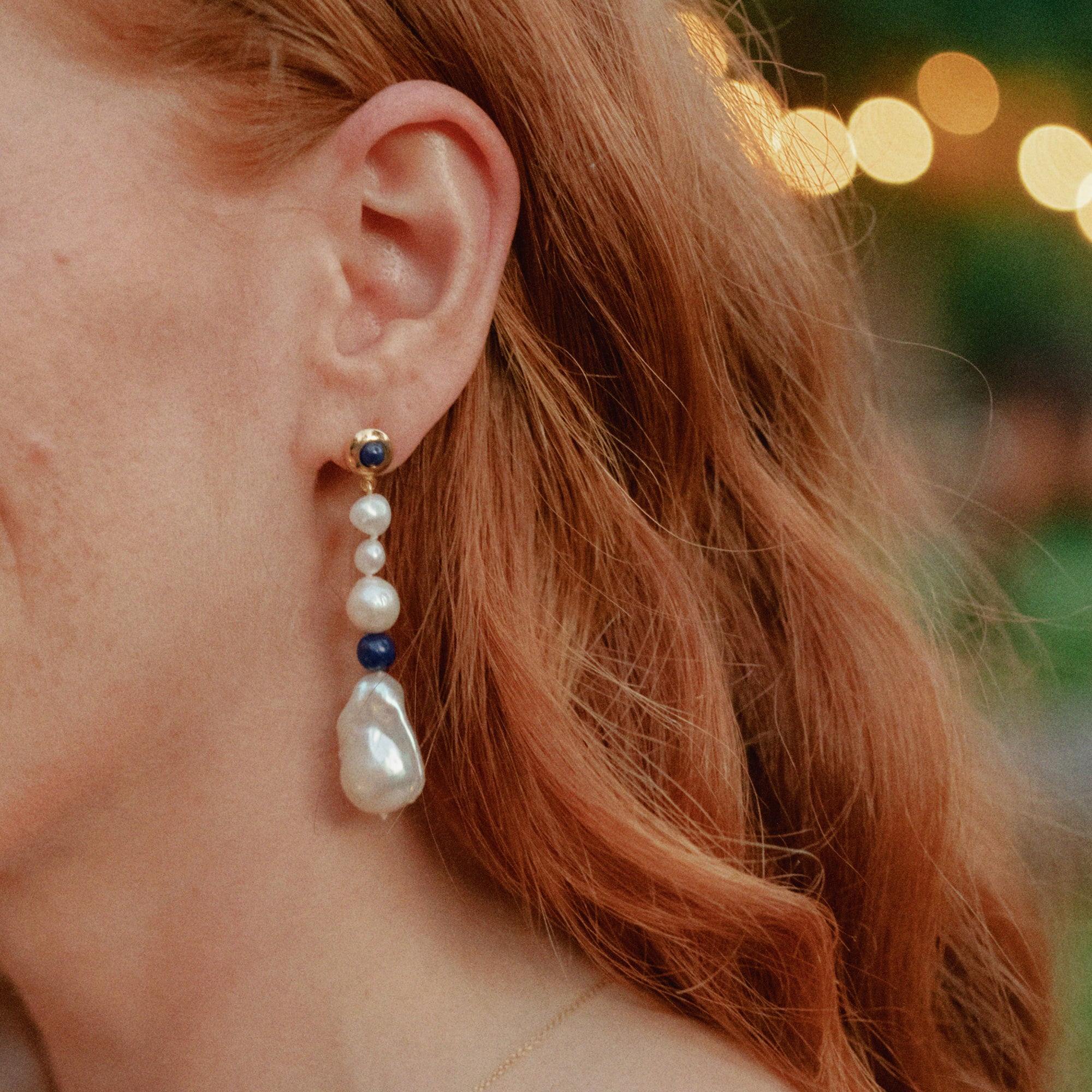 Person wearing AGMES 18K Gold Vermeil Kait Earrings with Baroque Pearl and Lapis Stone drop.