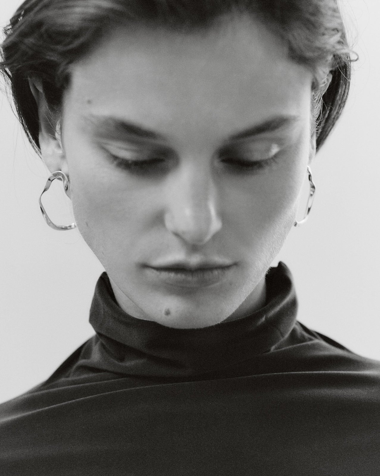 Woman wearing AGMES 18k gold vermeil sculptural wavy small round hoop earrings.
