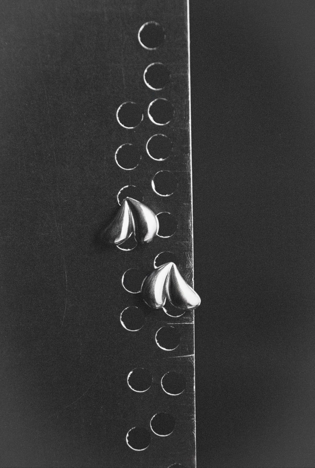 AGMES .925 sterling silver Lilla heart shaped earrings. On black background with earrings hung through holes in grey paper.