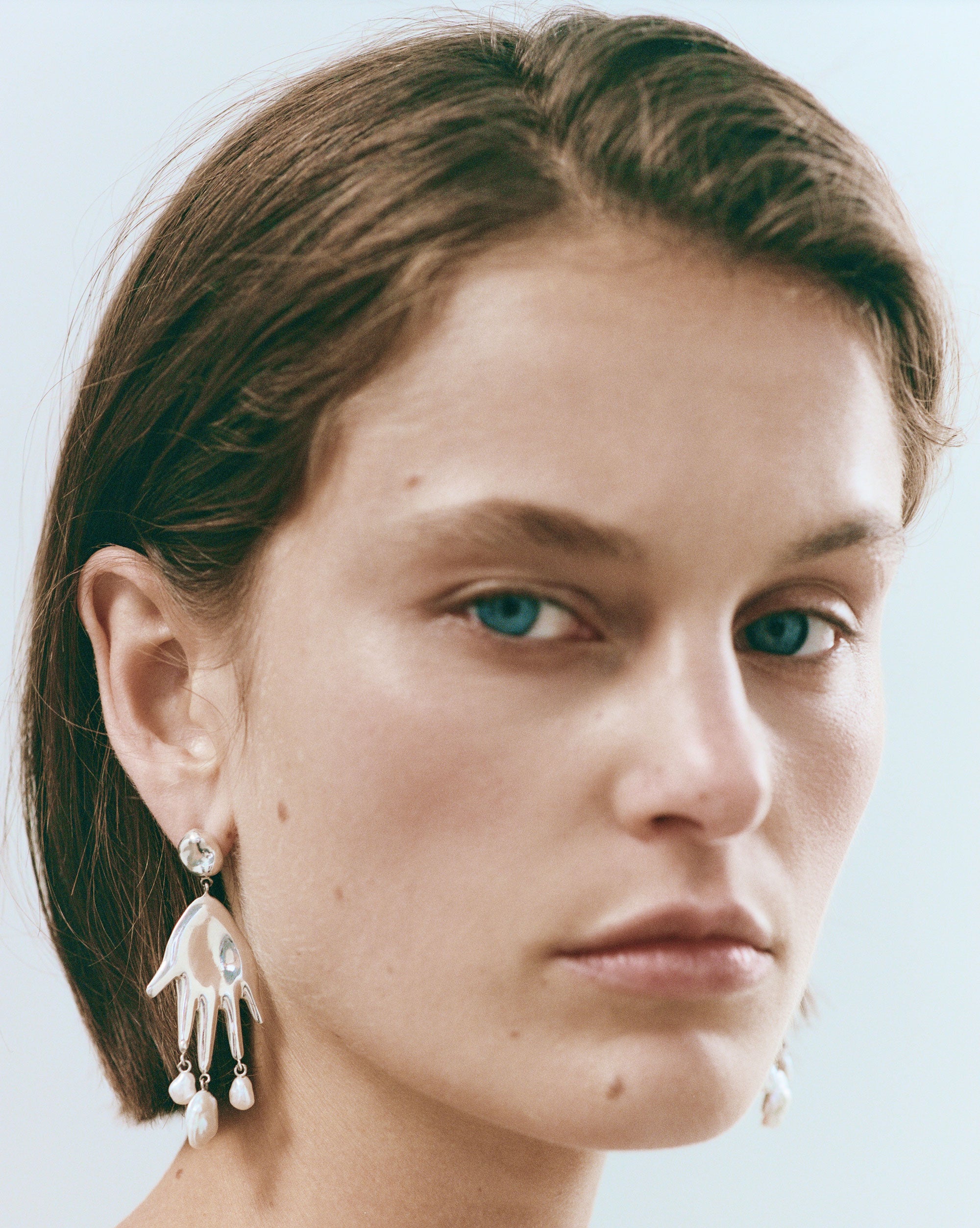 Woman wearing AGMES 0.925 sterling silver hand shaped earrings with freshwater pearl drops.