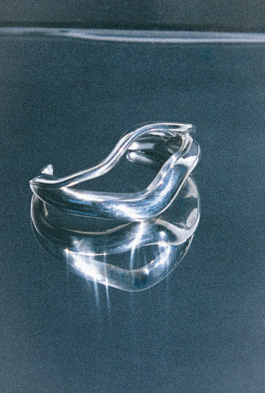 AGMES .925 sterling silver wavy sculptural Linnea cuff. On reflective blue background.