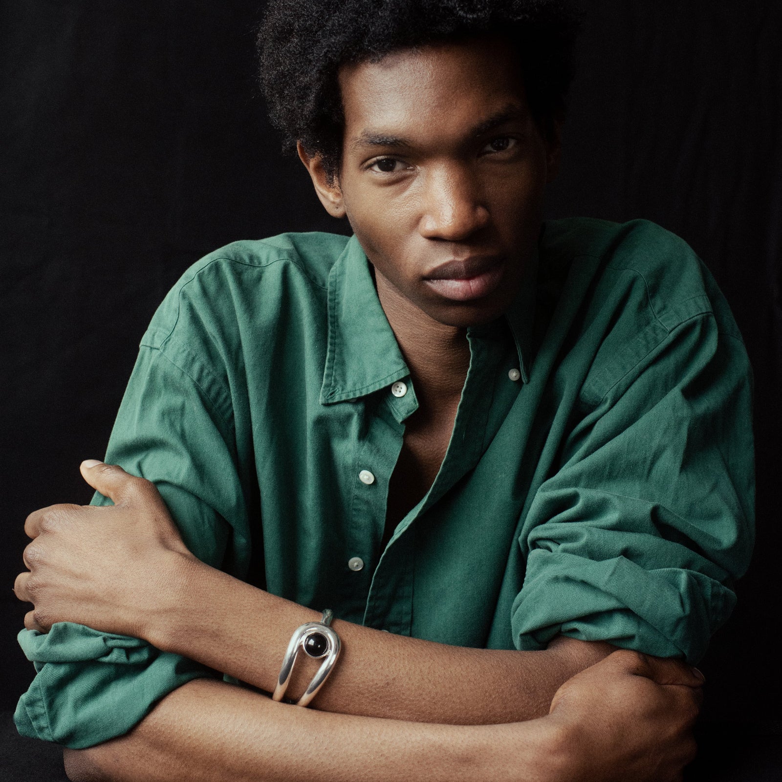 Person wearing green shirt and AGMES 0.925 sterling silver cuff bracelet with onyx stone in front of black background.