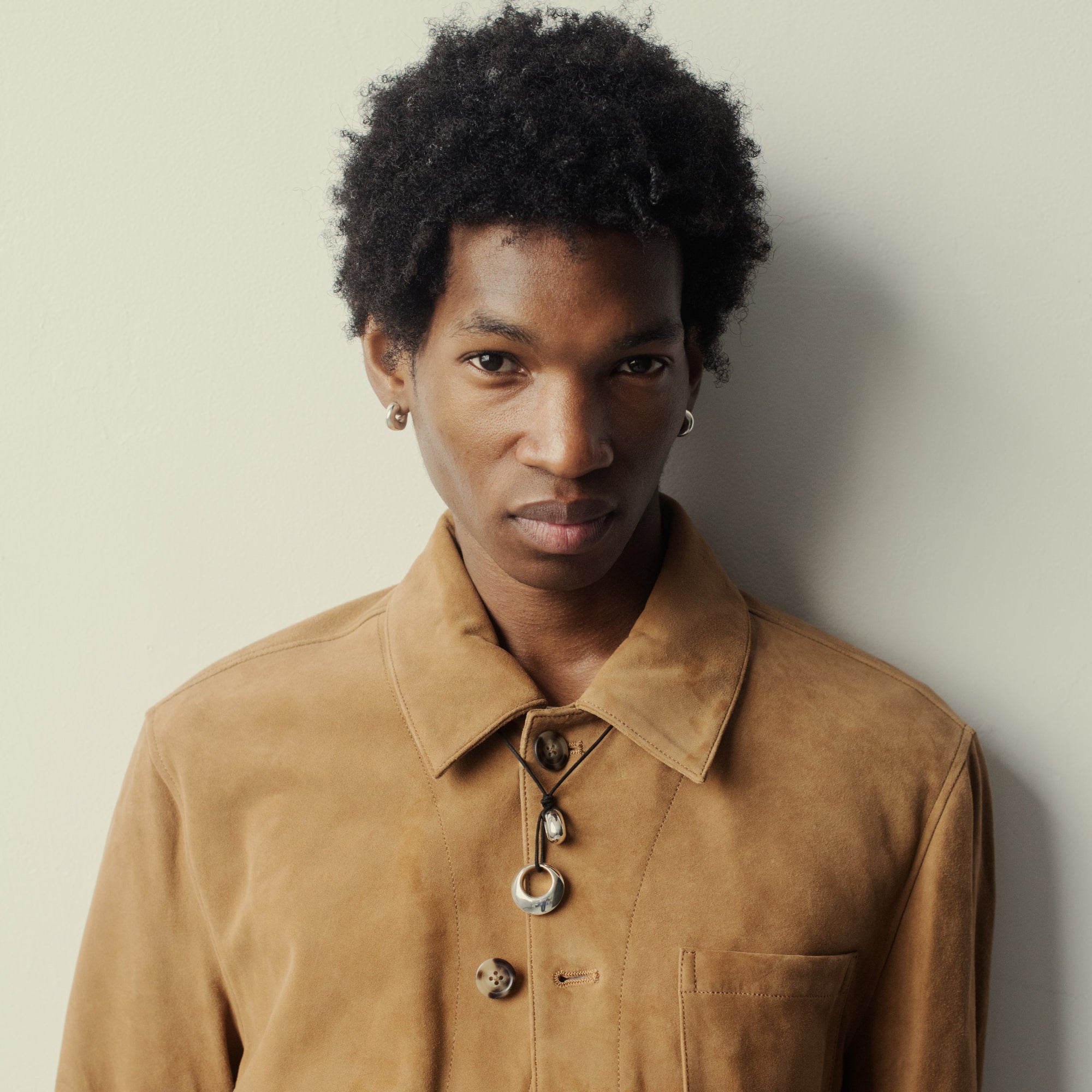 Man wearing AGMES 0.925 Sterling Silver Rae Pendant with Black Suede Cord over a brown suede jacket. 