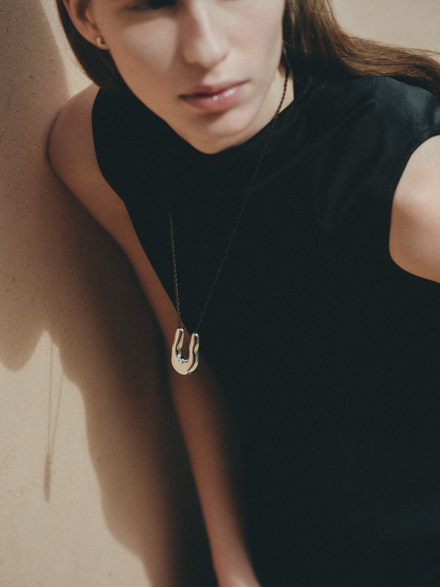 Woman wearing AGMES 925 sterling silver wishbone pendant on chocolate silk cord.