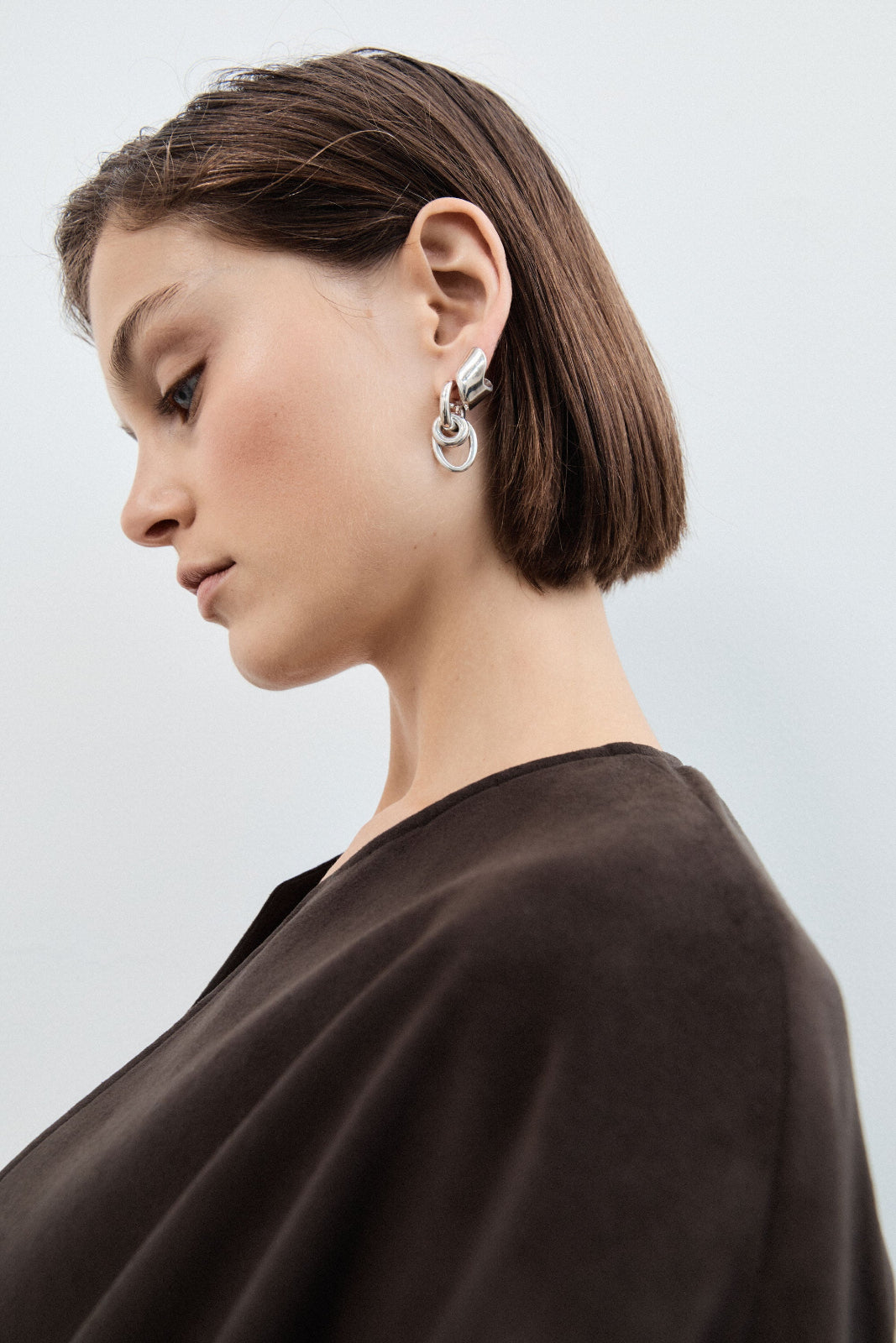 Woman wearing the AGMES .925 Sterling Silver Nelle Hoop Earrings. Asymmetrical mirrored hoops. 