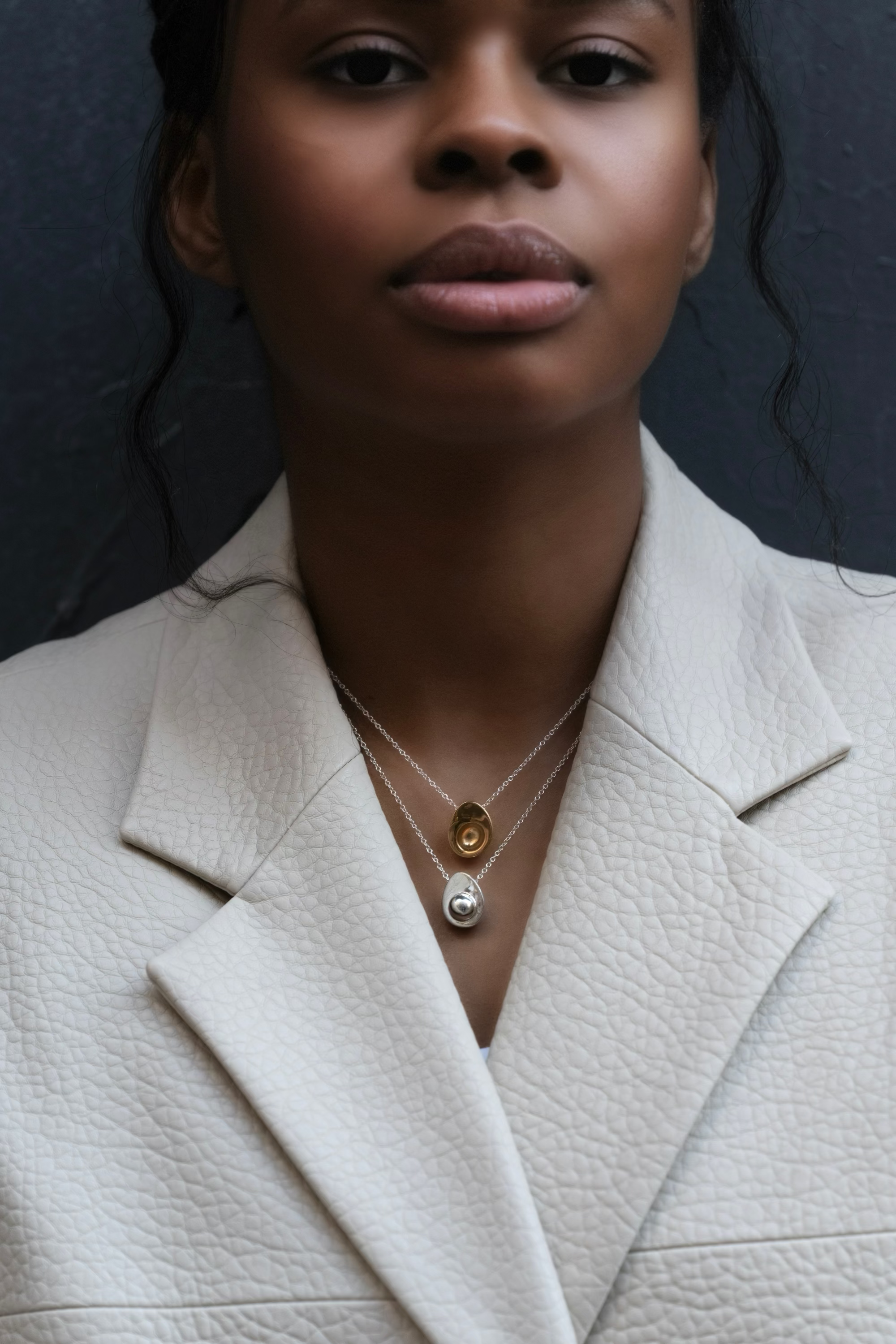 Woman in white leather blazer wearing AGMES 0.925 sterling silver avocado and  18k gold vermeil egg necklace. 
