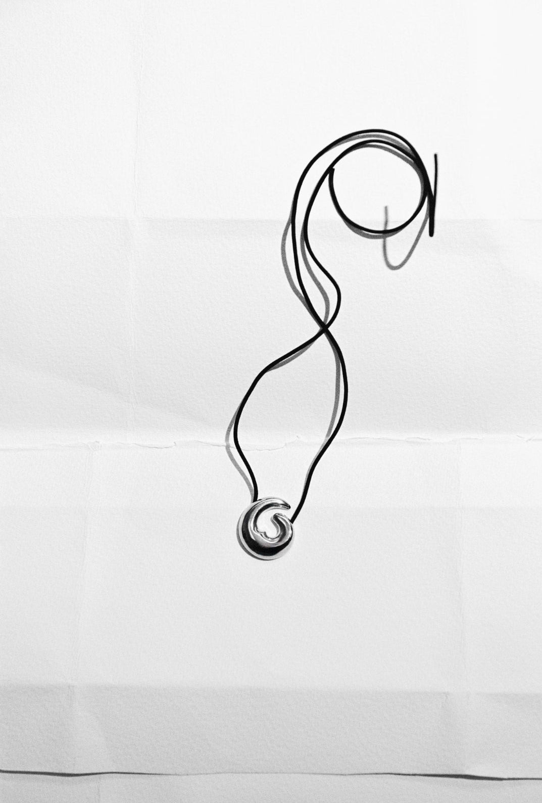 .925 sterling silver AGMES Nadia Pendant with Black Suede Cord laying on piece of paper, still life