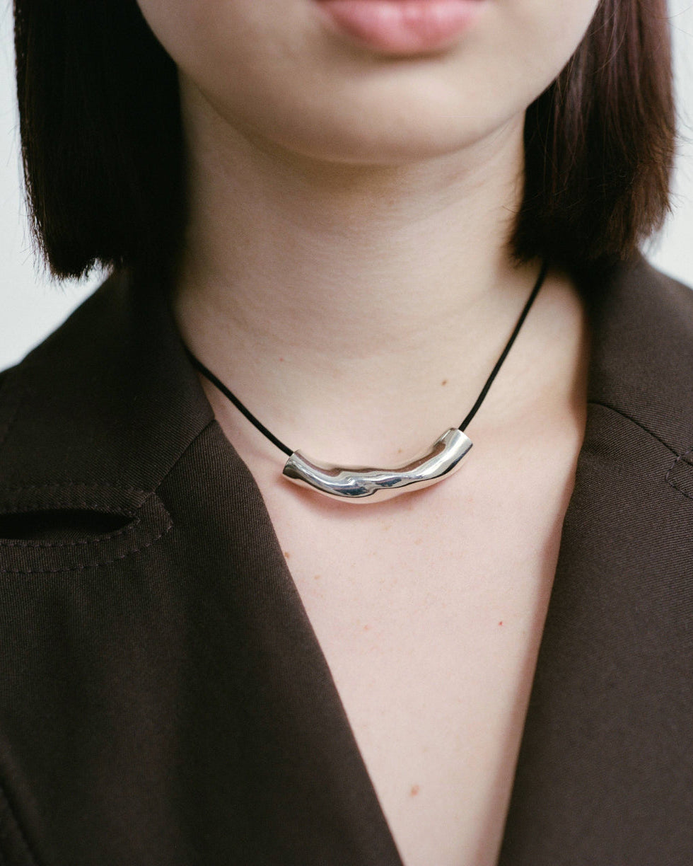 Model wearing AGMES .925 sterling silver sculptural round twisted Small Astrid Pendant on black suede cord.