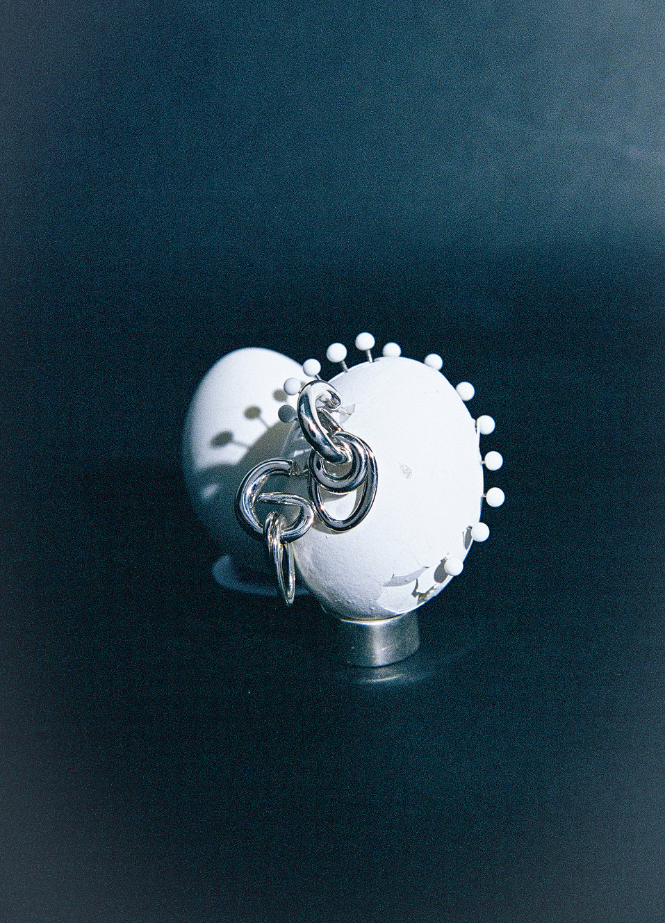 AGMES .925 sterling silver sculptural layered hoop Ellipses Earrings attached to white egg on dark blue background.