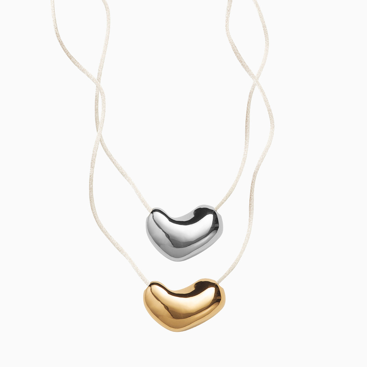 silver sculpted heart pendant and gold pendant necklaces with ivory cords on a white background