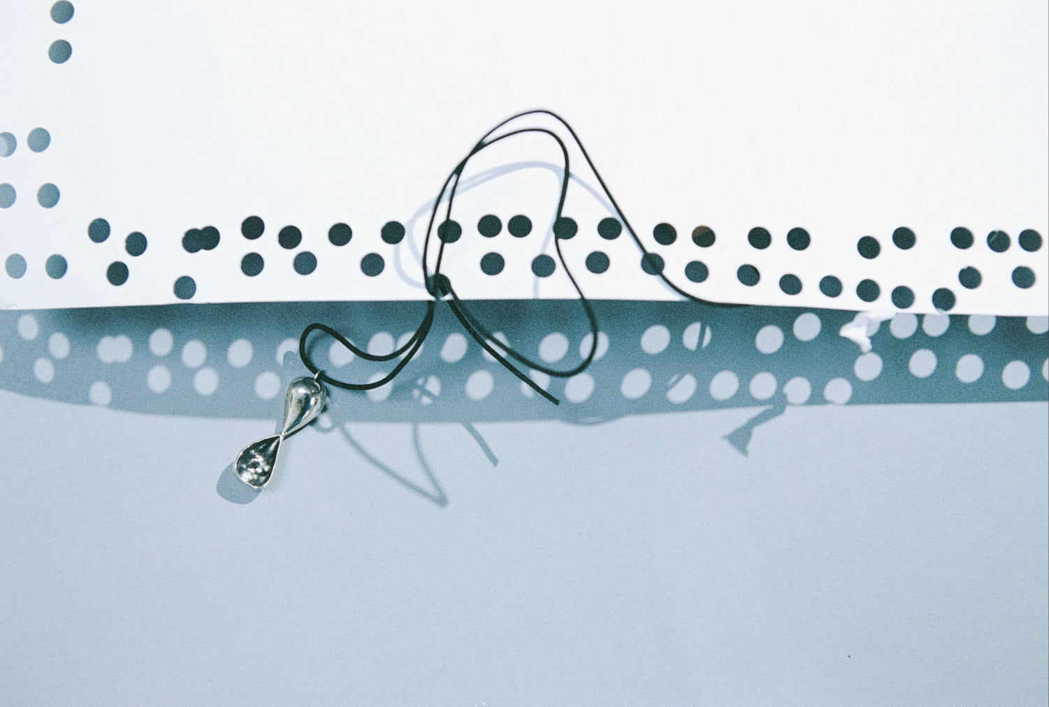 AGMES .925 sterling silver Inti infinity shaped pendant necklace on black suede cord. Pendant is on light blue background with cord string through holes in white paper.
