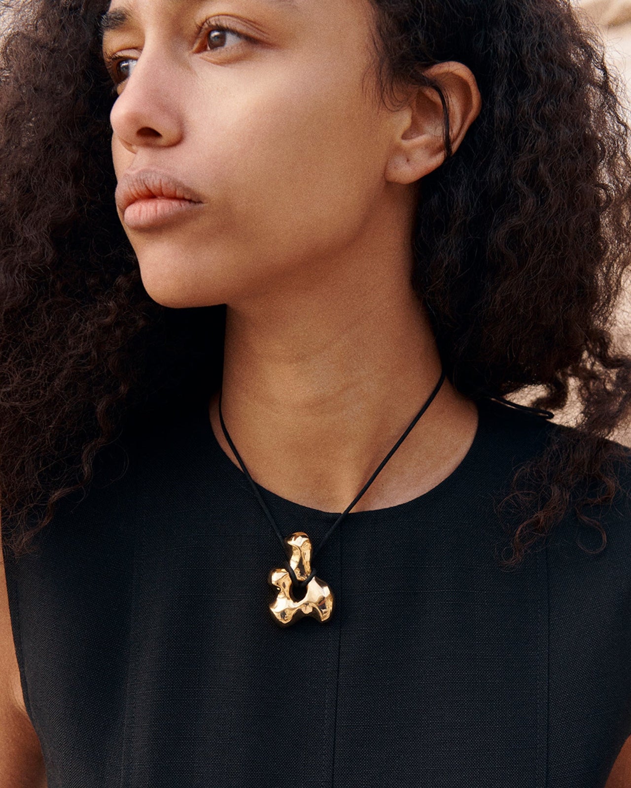 Woman wearing AGMES 18k Gold Vermeil sculpted pendant on black suede cord. Simone Bodmer-Turner.