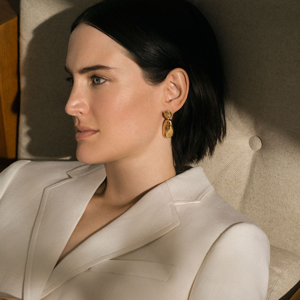Woman wearing 18k gold vermeil sculpted round drop earrings.