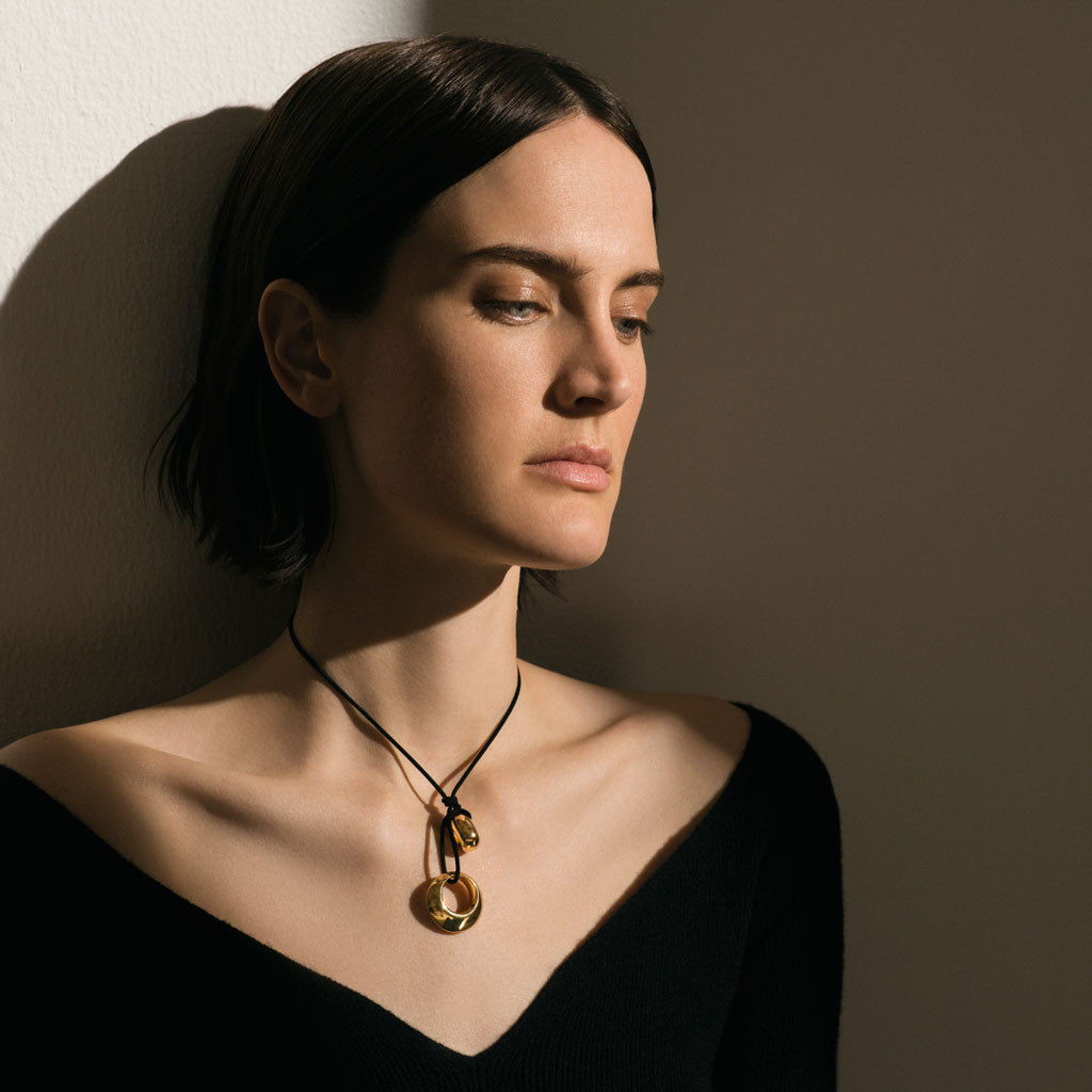 Woman wearing AGMES 18k Gold Vermeil Sterling Rae Pendant with Black Suede Cord necklace with black blouse.