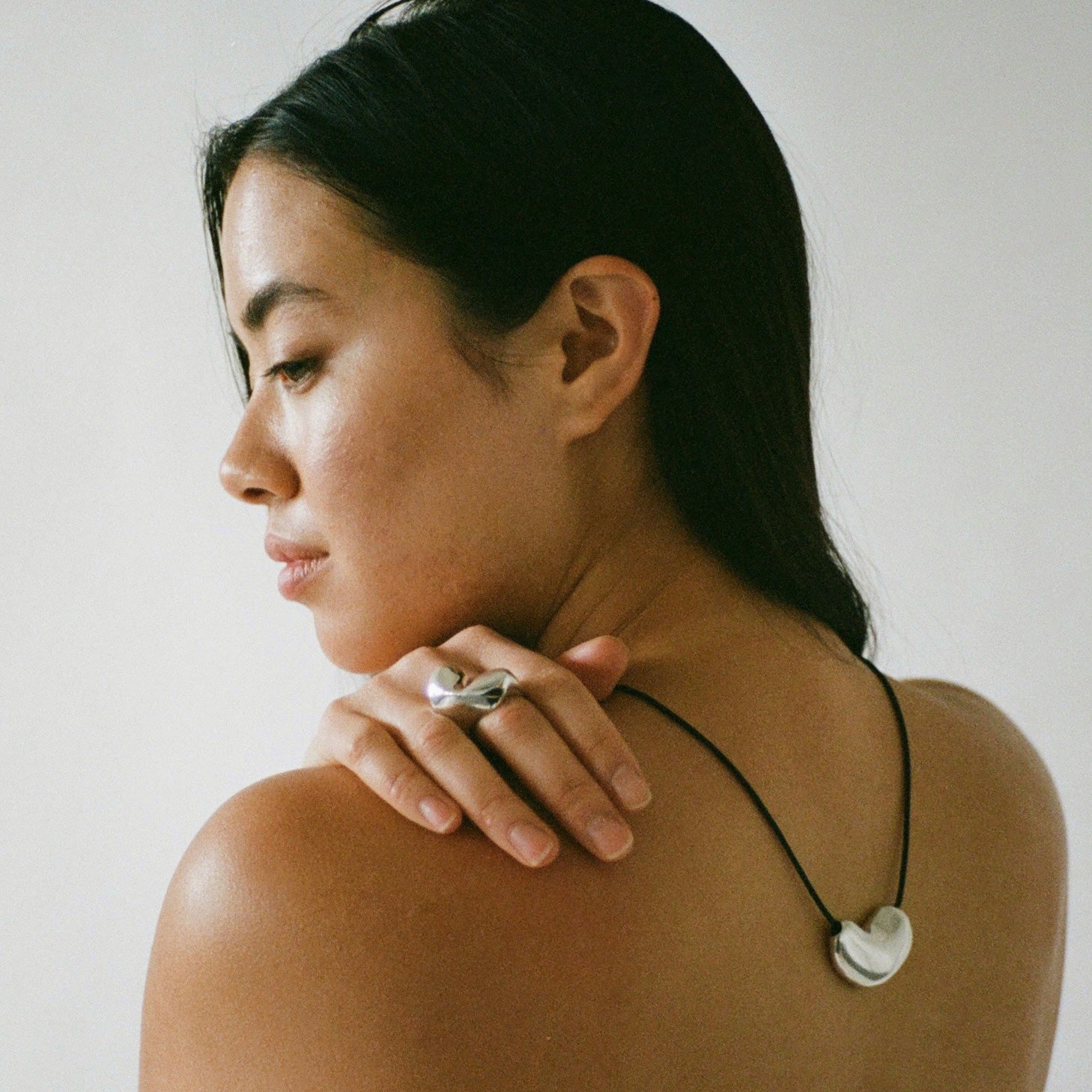 Woman wearing AGMES .925 Sterling Turner Ring and Silver Sculpted Heart Pendant on Black Suede Cord. 