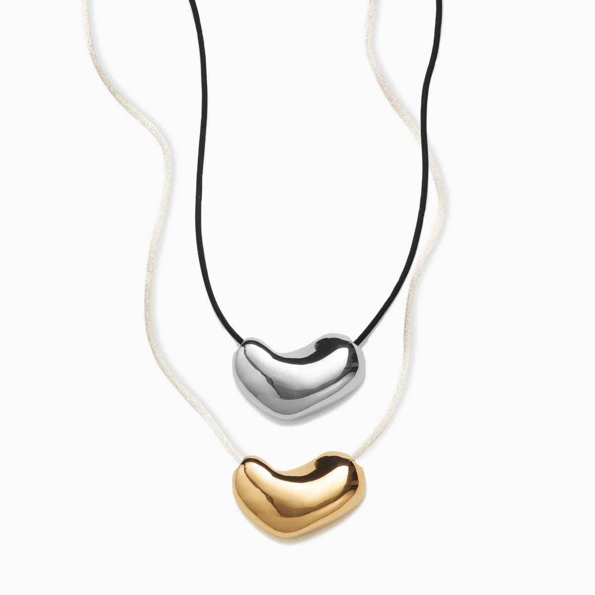 AGMES Sculpted Heart Pendant Set. 925 Sterling Silver Sculpted Heart Pendant on Black Suede Cord paired in a set with 18K Gold Vermeil Sculpted Heart Pendant on Ivory Satin Cord. 