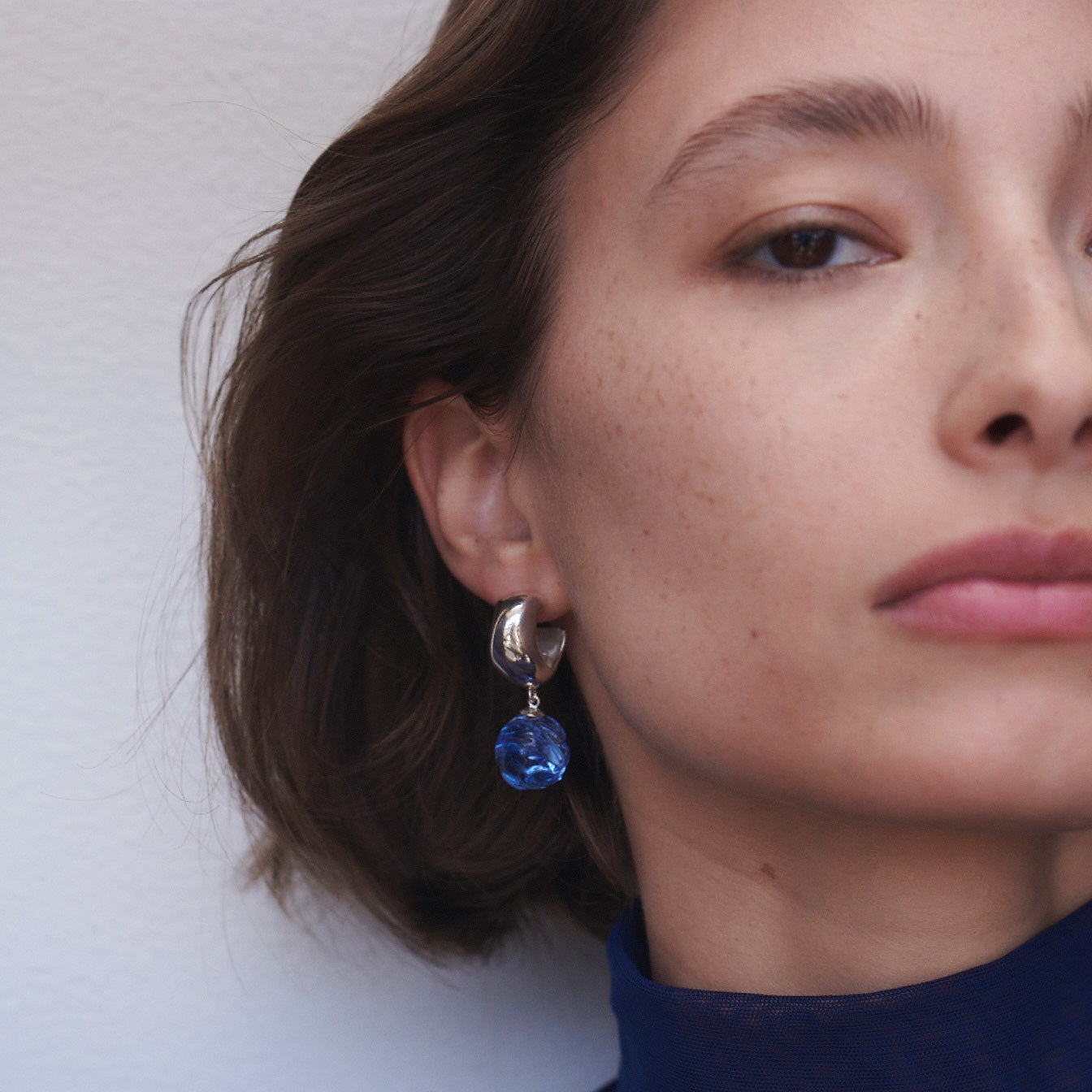 Woman wearing AGMES 0.925 sterling silver small Cleo hoop earrings with blue glass bead drop.