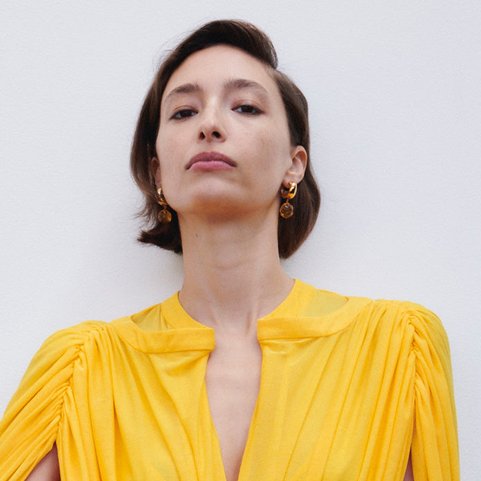 Woman wearing AGMES yellow gold small Cleo hoop earrings with yellow glass bead drop.