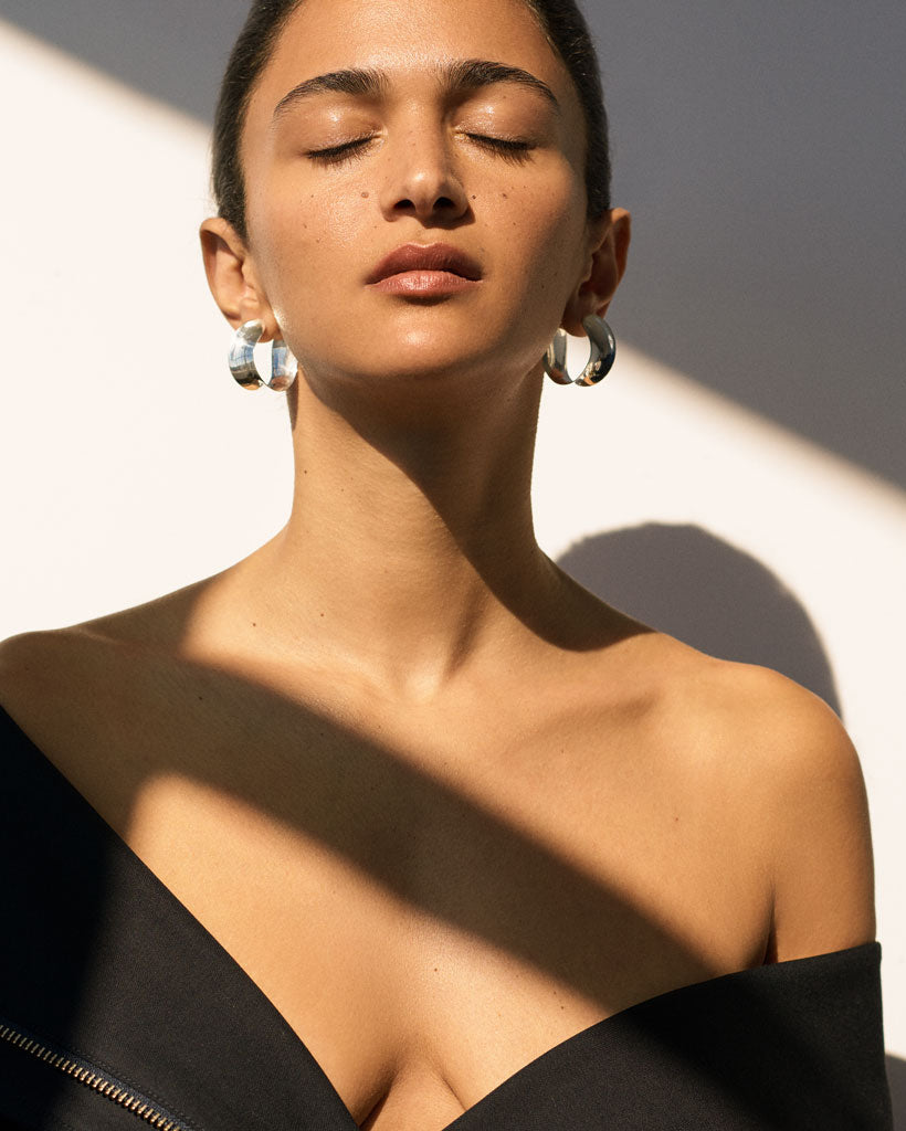 Woman wearing AGMES 0.925 sterling silver Laila twist hoop earrings.