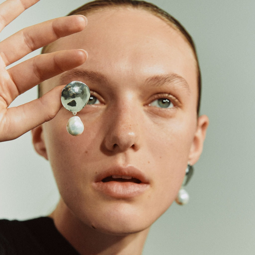 Woman holding AGMES 0.925 sterling silver disc earrings with freshwater pearl drop.