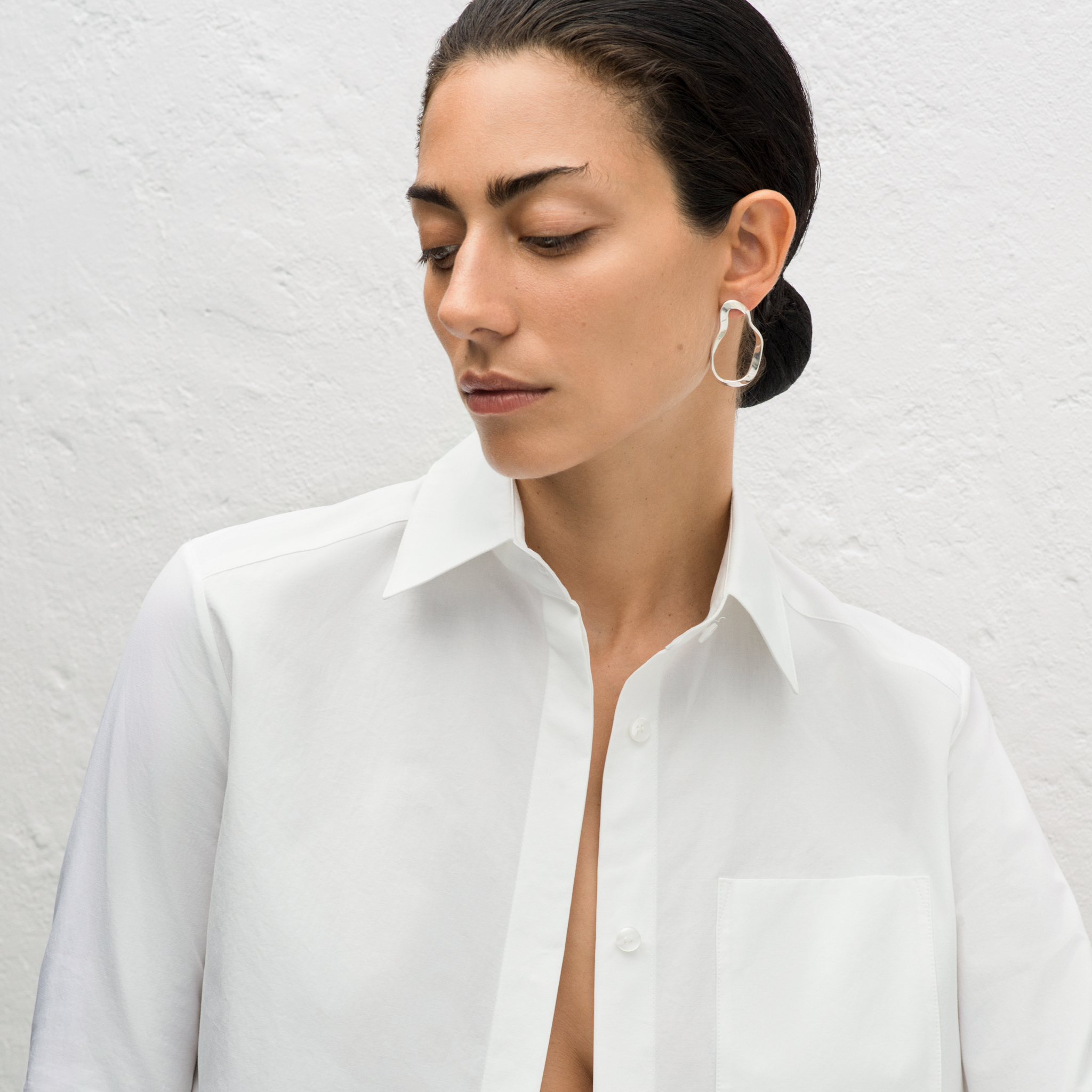 Woman wearing AGMES 0.925 sterling silver sculptural wavy small round hoop earrings.