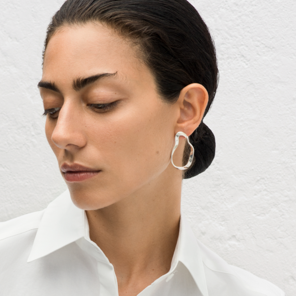 Woman wearing AGMES 0.925 sterling silver sculptural wavy small round hoop earrings.