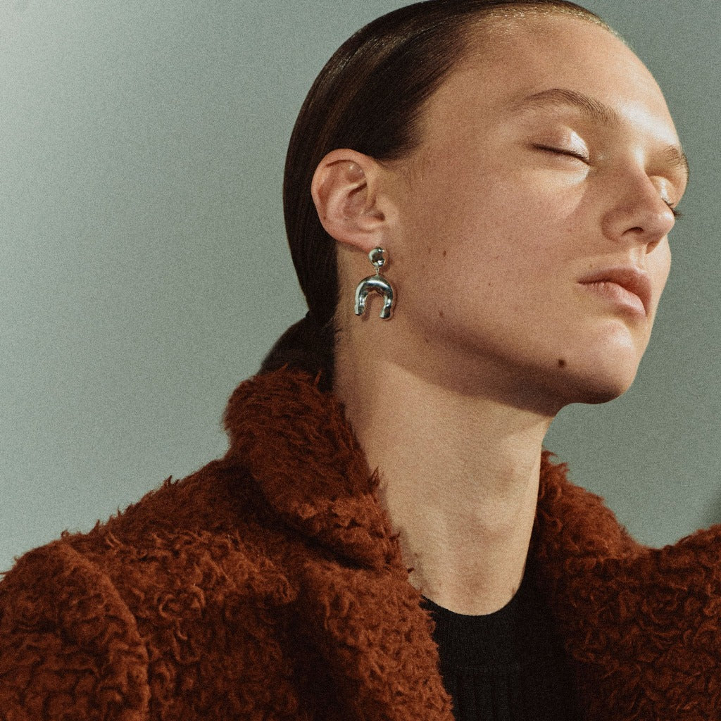 Woman wearing AGMES 0.925 sterling silver earrings with sculpted wishbone drop.