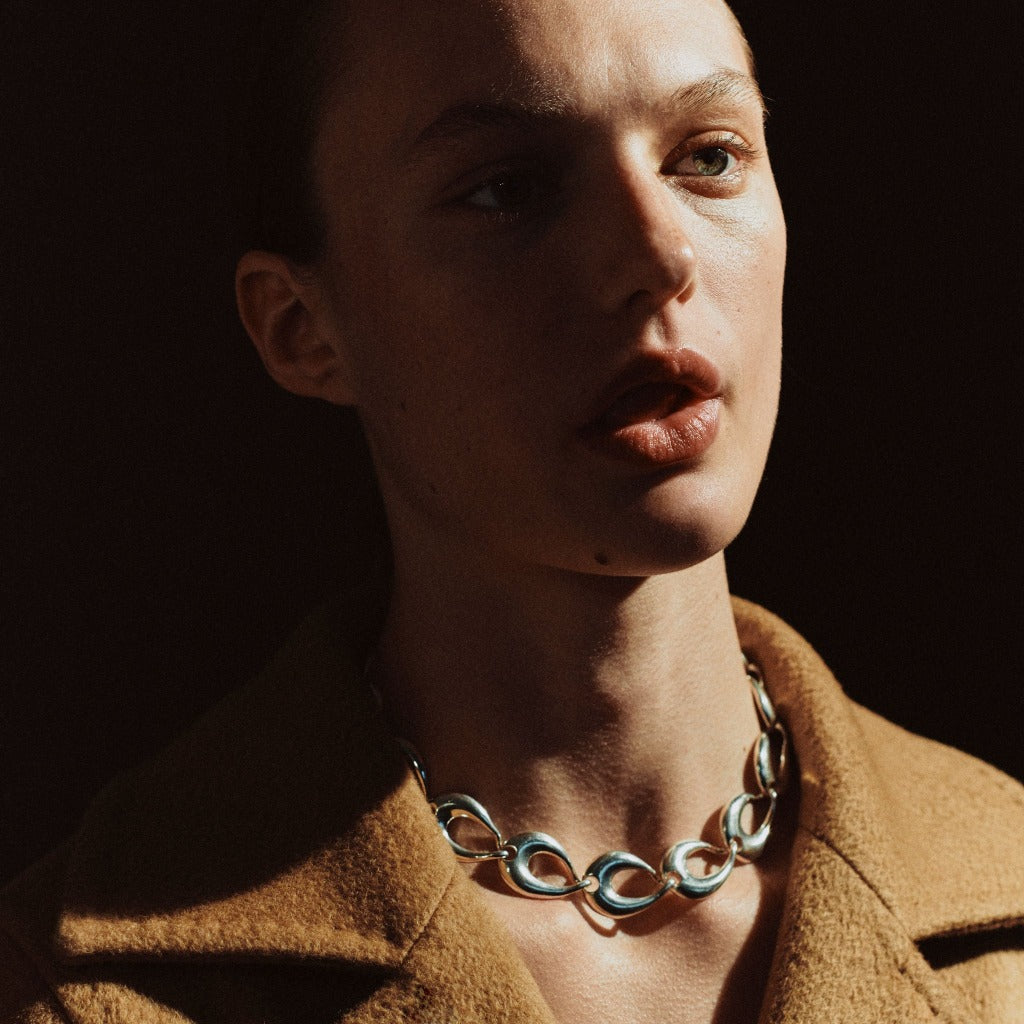 Model wearing AGMES .925 sterling silver sculptural link Tilda Necklace and tan coat.