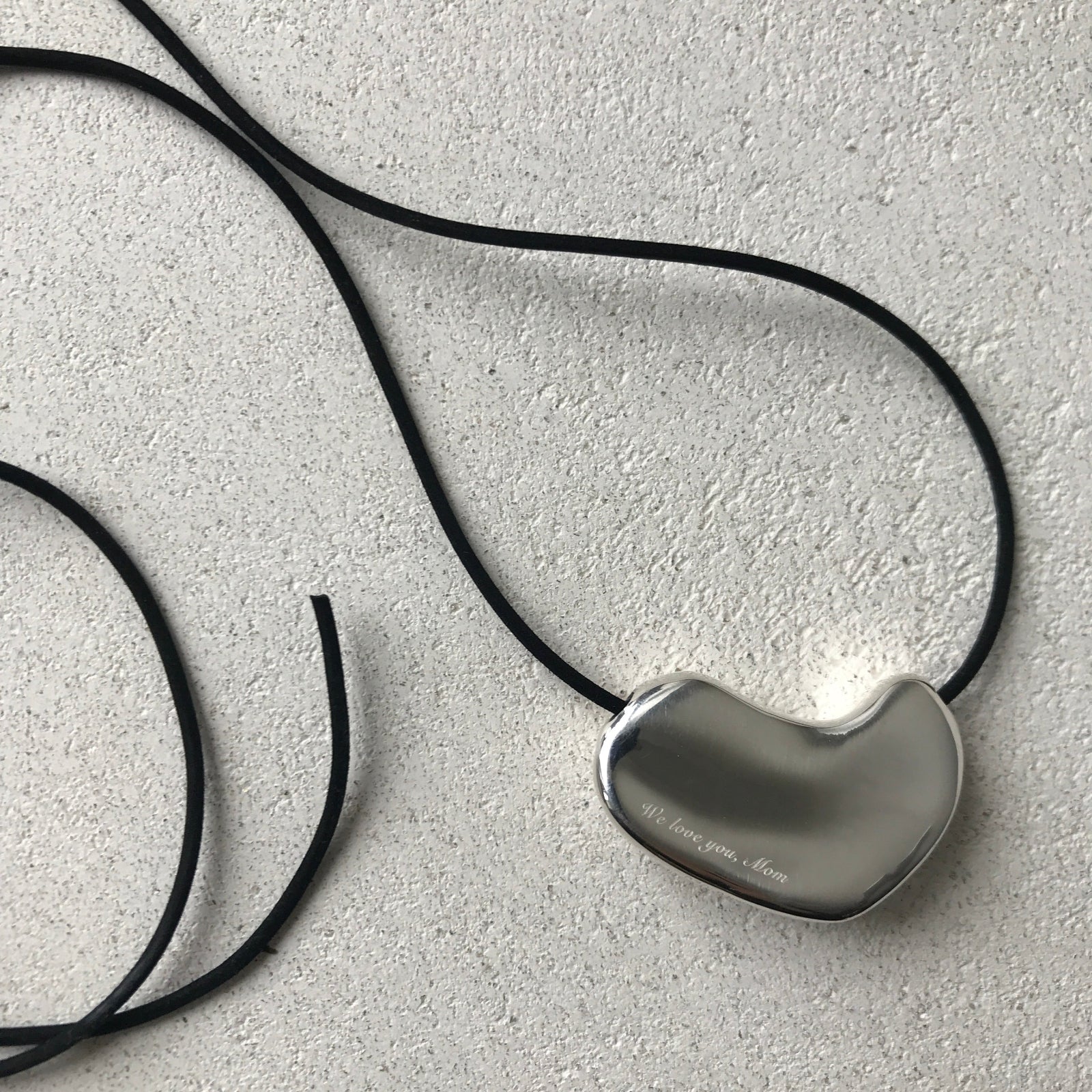 AGMES .925 Sterling Silver Sculpted Heart Pendant with script engraving on Black Suede Cord on white speckled background. 