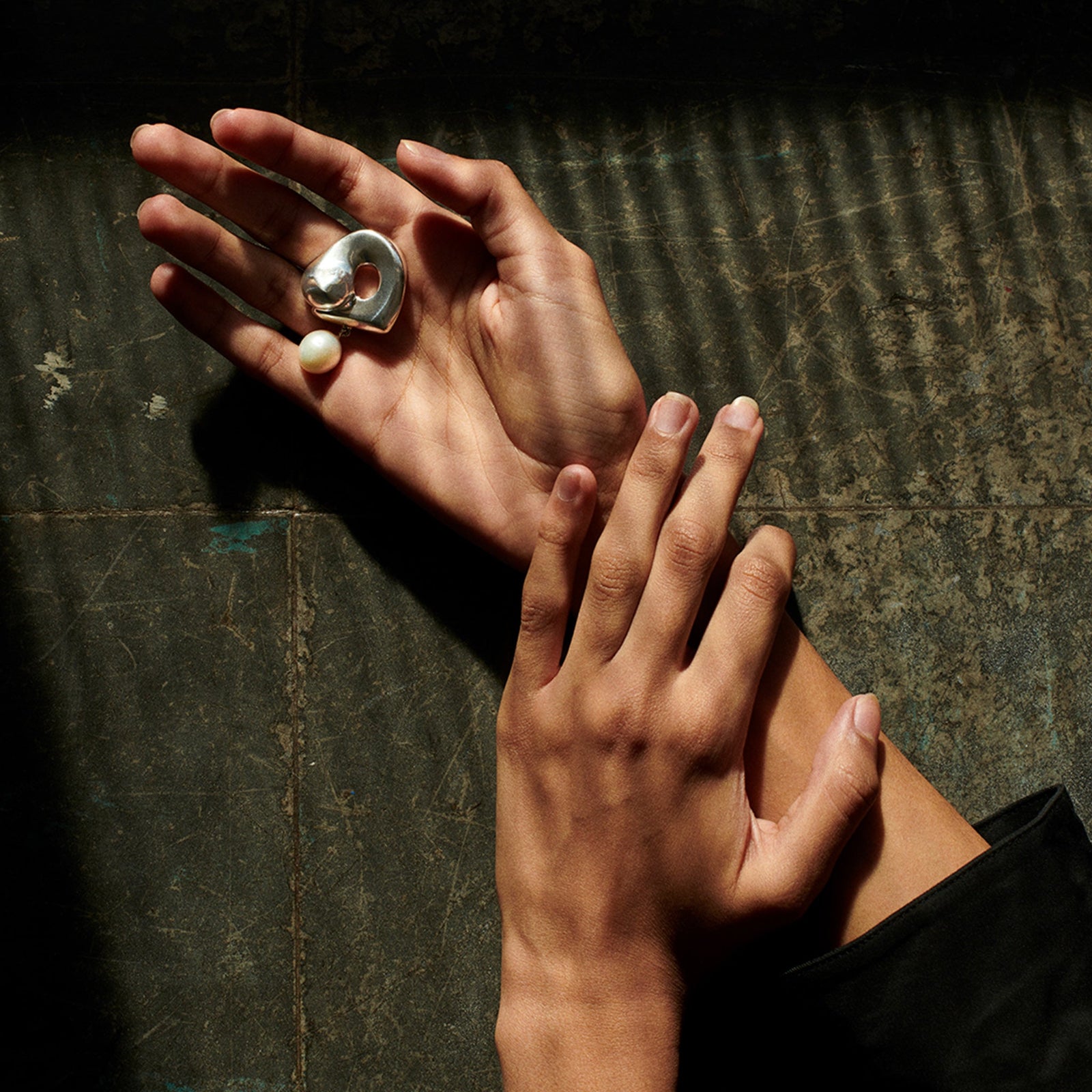 Hand holding AGMES 0.925 sterling silver sculpted Gertrude pearl drop earrings. Simone Bodmer-Turner.